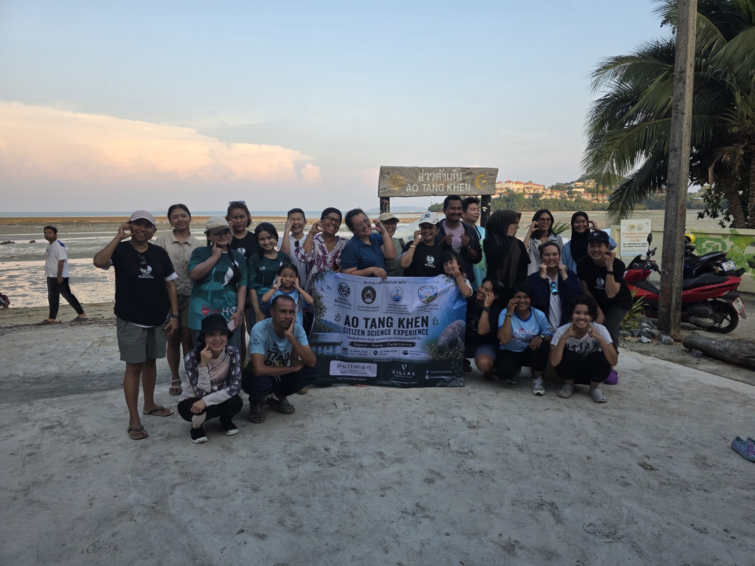 Group of citizen science participants holding the AO TANG KHEN Citizen Science Experience banner on the beach